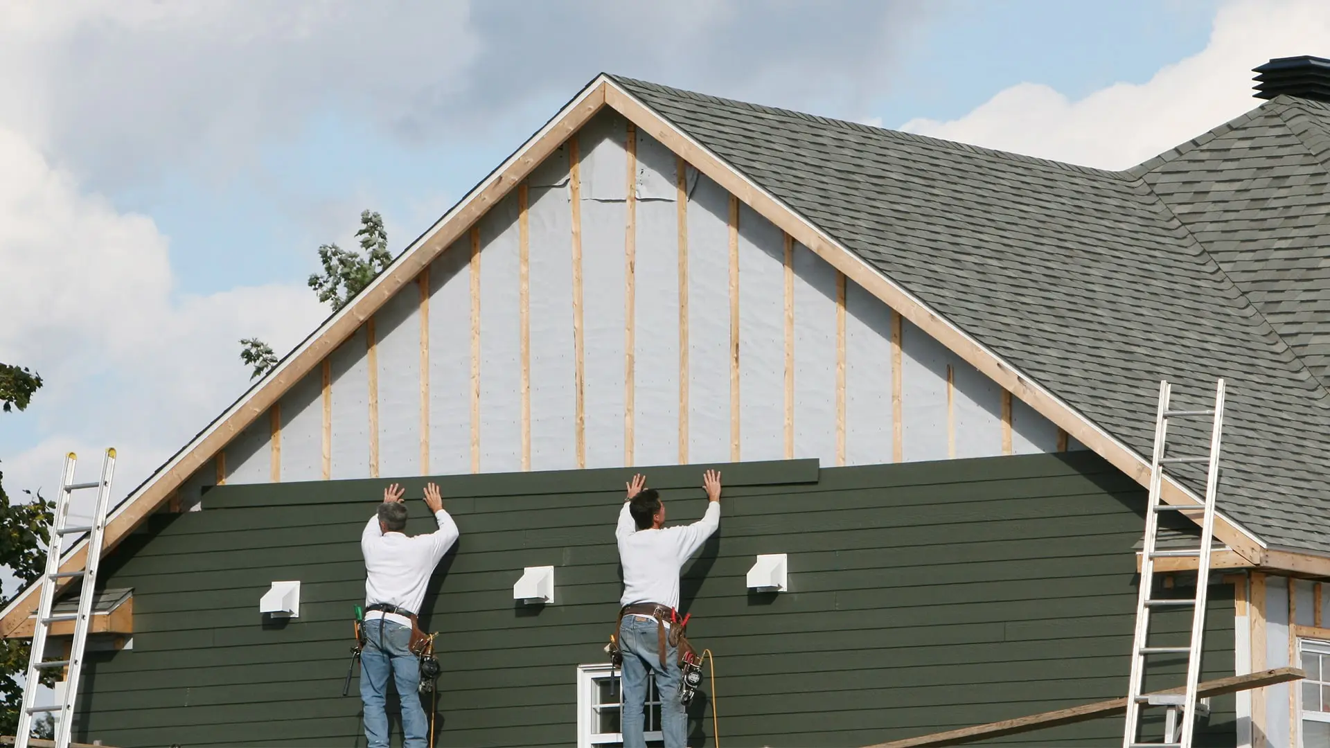 Siding contractor installing fiber cement panels on a suburban home